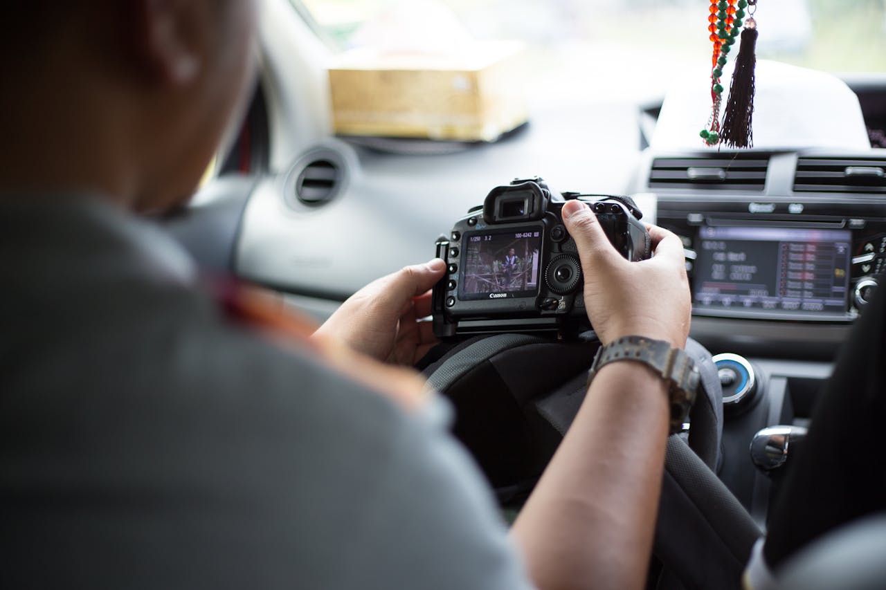 Photographer holding DSLR camera inside car, checking images and settings.
